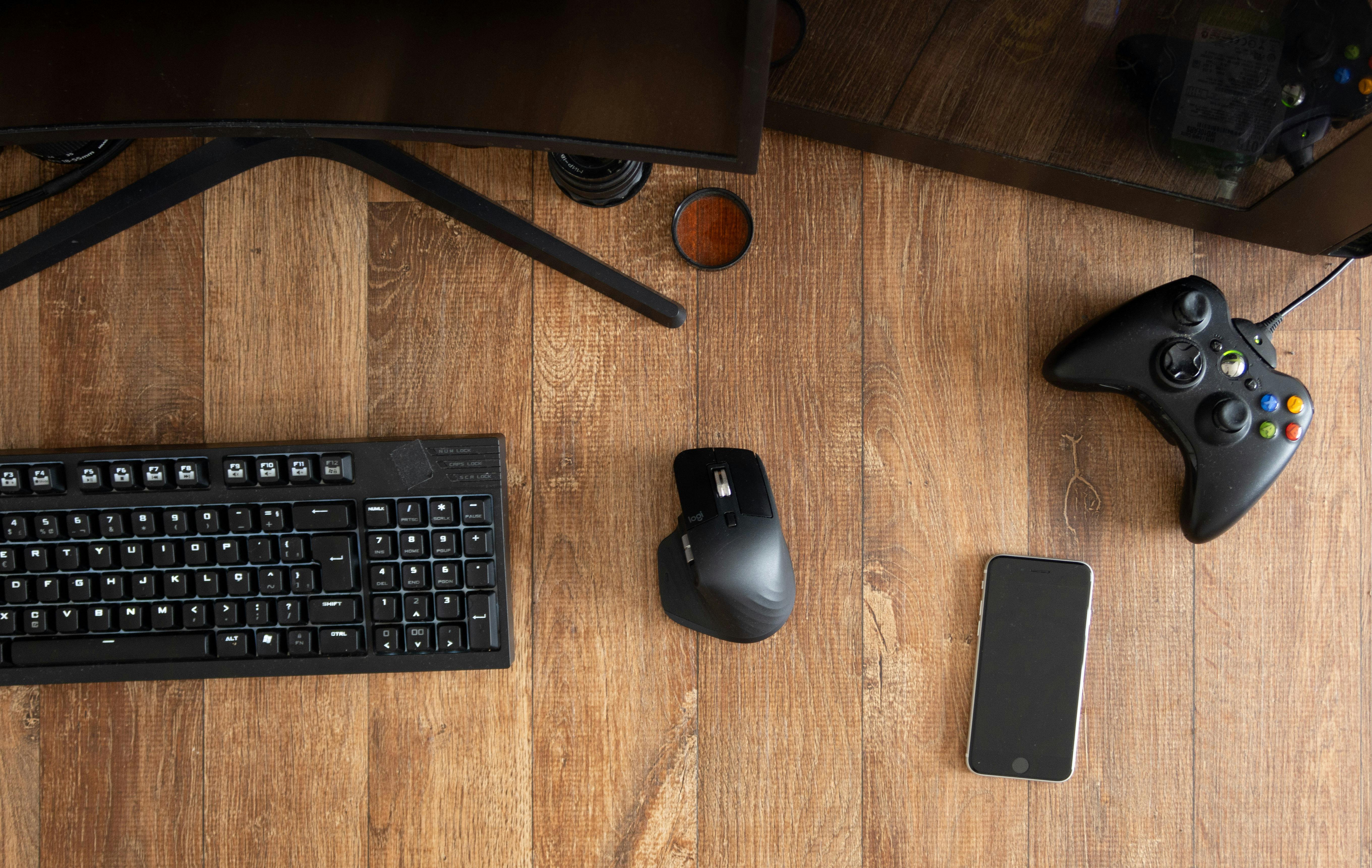 Top view of black gamepad with mouse and keyboard on wooden desk with monitor in apartment in daytime