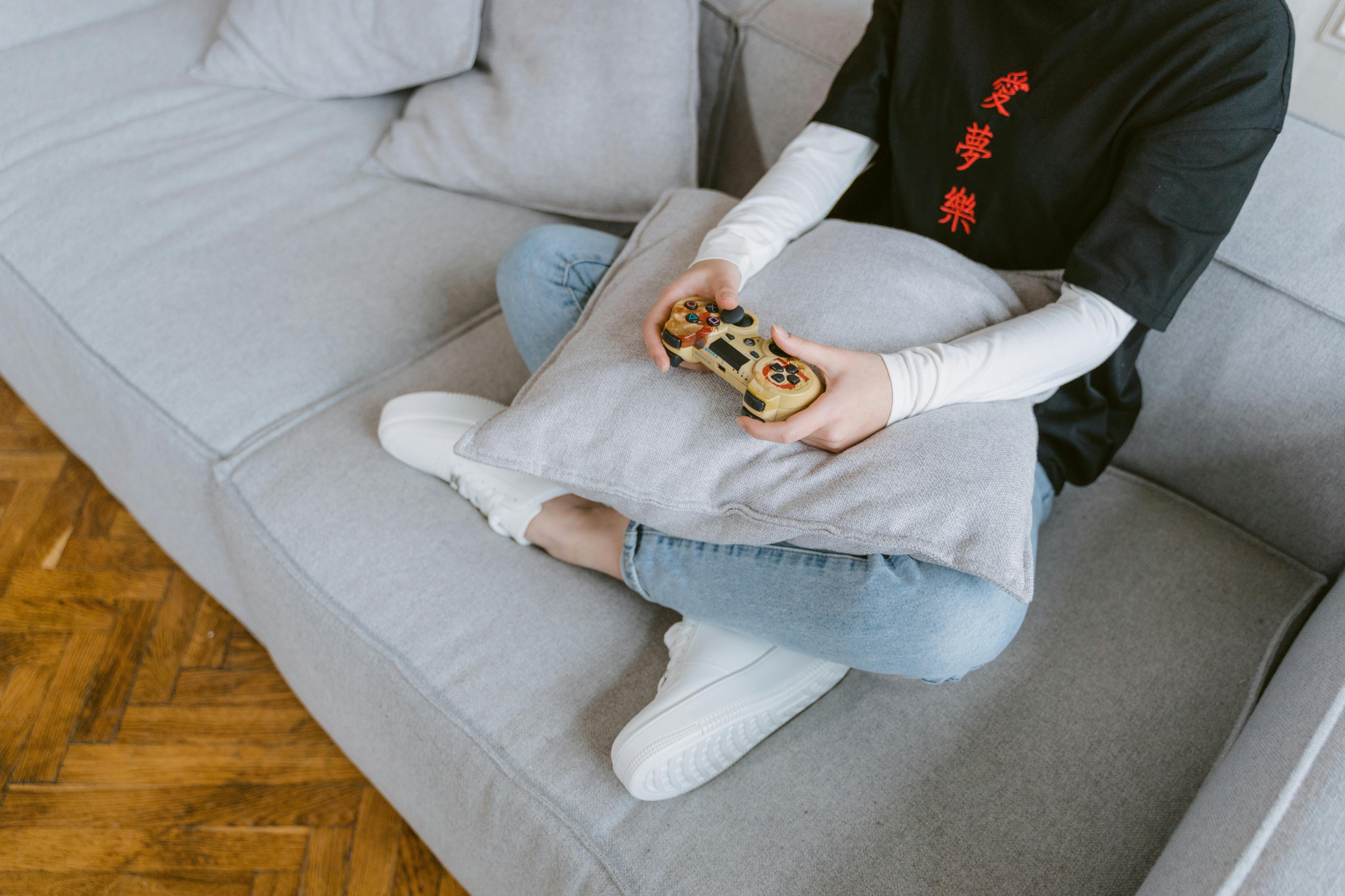Person sitting on a couch playing video games, symbolizing leisure and entertainment.